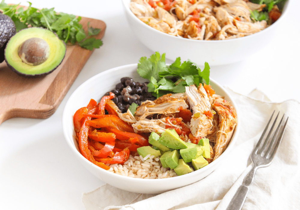 Instant Pot mexican chicken in a white bowl with avocados in the background
