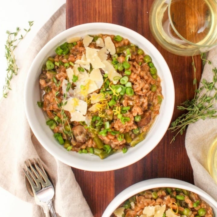 farro risotto in a bowl with mushrooms and asparagus topped with grated parmesan cheese