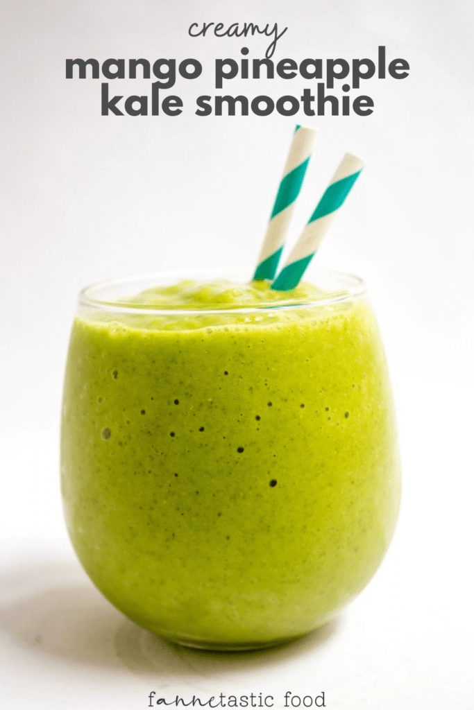 mango pineapple smoothie with kale in a glass with striped straws