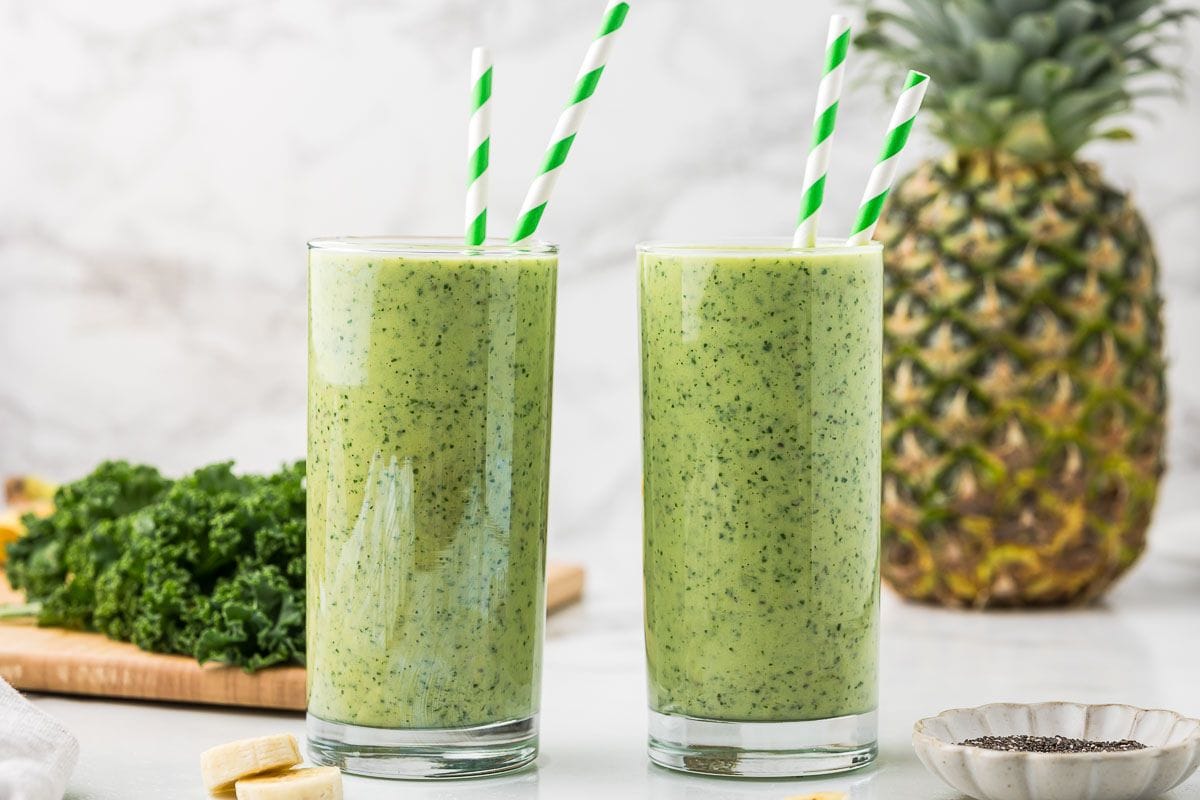 two mango pineapple green smoothies with kale in tall glasses with a pineapple in the background