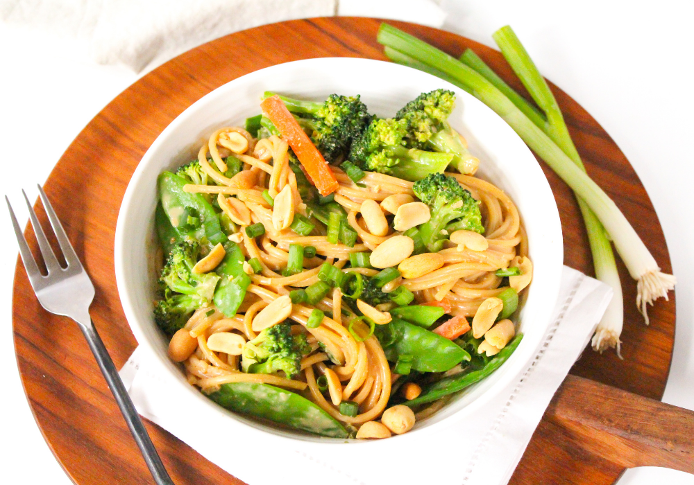 veggie pasta with peanut sauce in a white bowl on a wooden platter