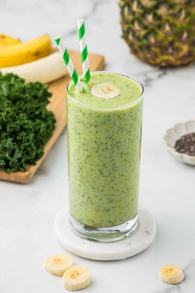 pineapple mango smoothie with kale in a tall glass with a sliced banana