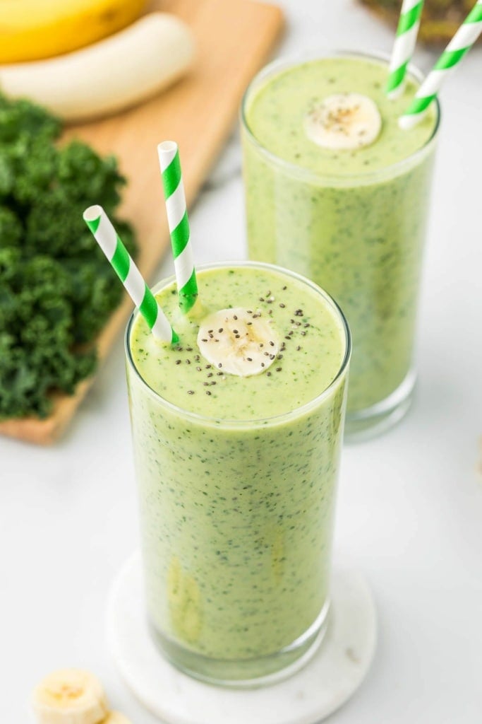 tropical kale fruit smoothie with banana in a tall glass with green striped straws