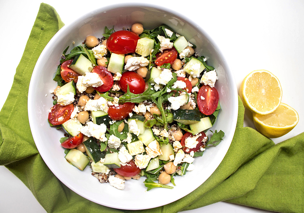 quinoa chickpea salad with feta in a white bowl with sliced lemons