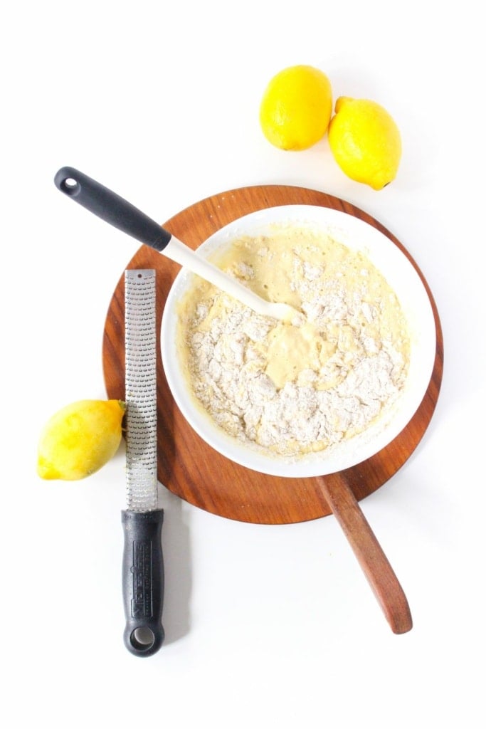 a white mixing bowl with pancake batter next to lemons and a metal zester