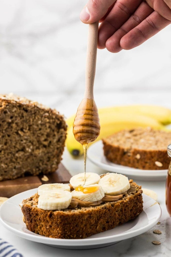 a slice of banana bread with peanut butter and honey being drizzled on top