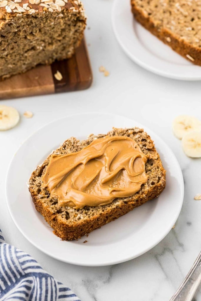 a slice of banana bread smeared with peanut butter on a plate