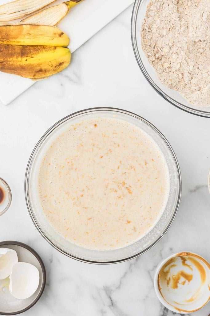 eggs, mashed bananas, milk, and more wet baking ingredients in a glass bowl