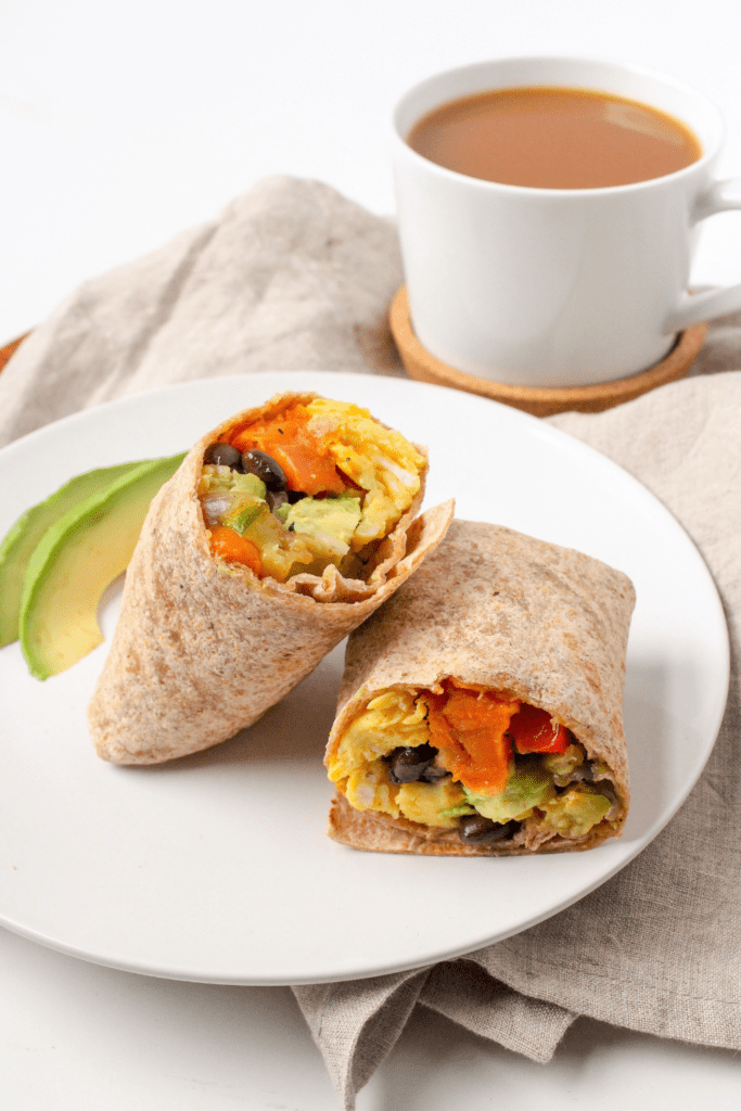 vegetarian breakfast burritos with sweet potato on a plate with a mug of coffee in the background