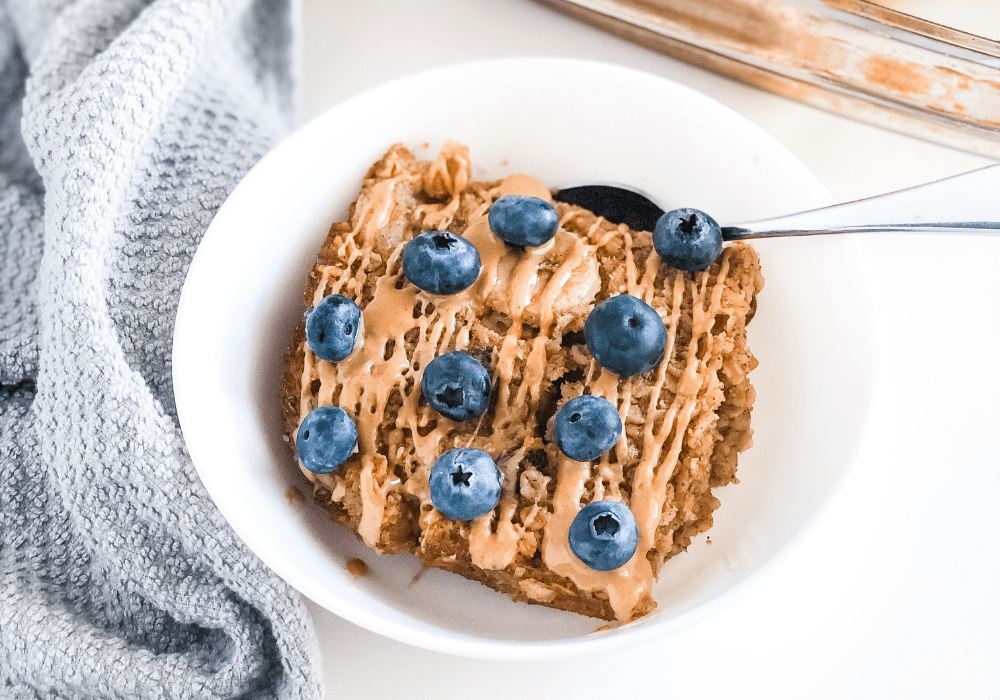 banana baked oatmeal in a white bowl with a grey kitchen towel beside it