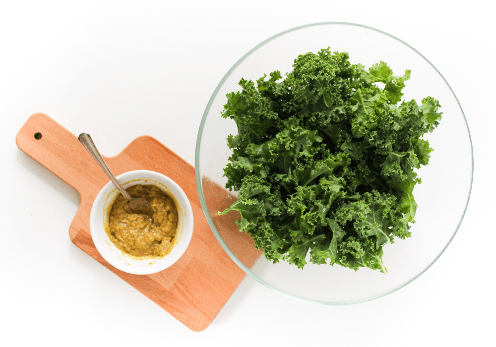 a bunch of kale with seasoning and tahini sauce in a small bowl beside it