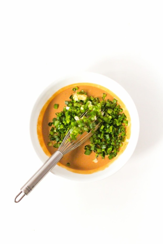 a bowl with peanut sauce and sliced green onions with a wire whisk