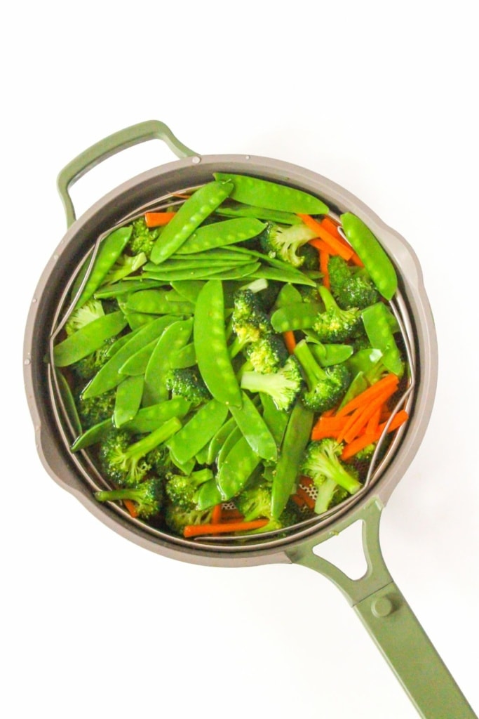 a strainer filled with broccoli, snow peas, and shredded carrots