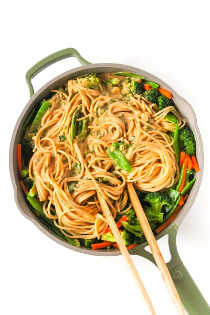 a large skillet filled with noodles and vegetables tossed in creamy peanut sauce