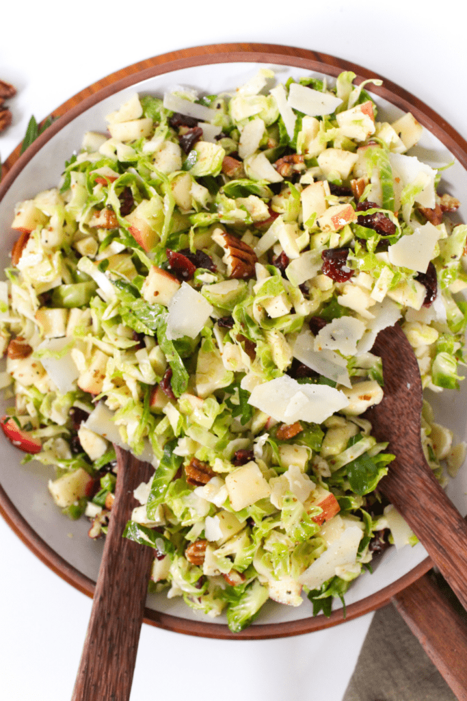 shaved brussels sprouts salad in a bowl with wooden spoons