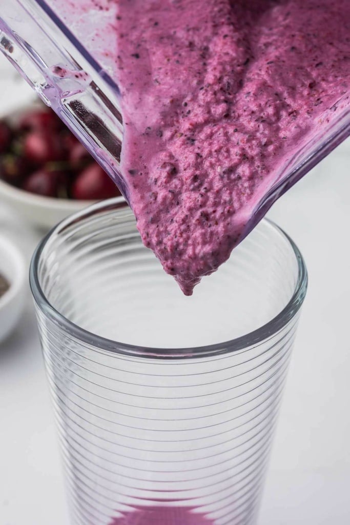 a purple smoothie being poured from a blender into a tall glass