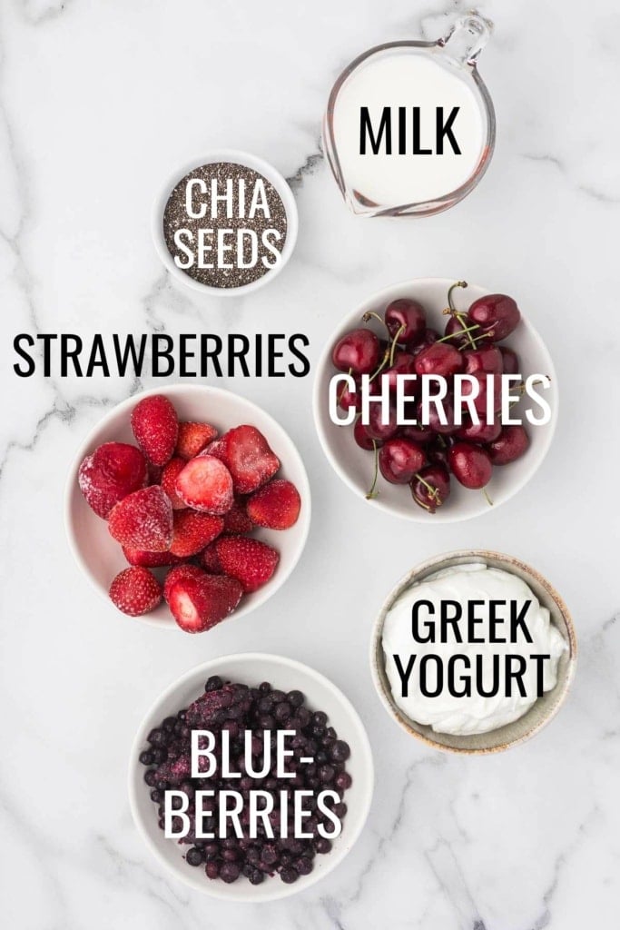 strawberries, blueberries, cherries, Greek yogurt, milk, and chia seeds in small bowls on a marble surface