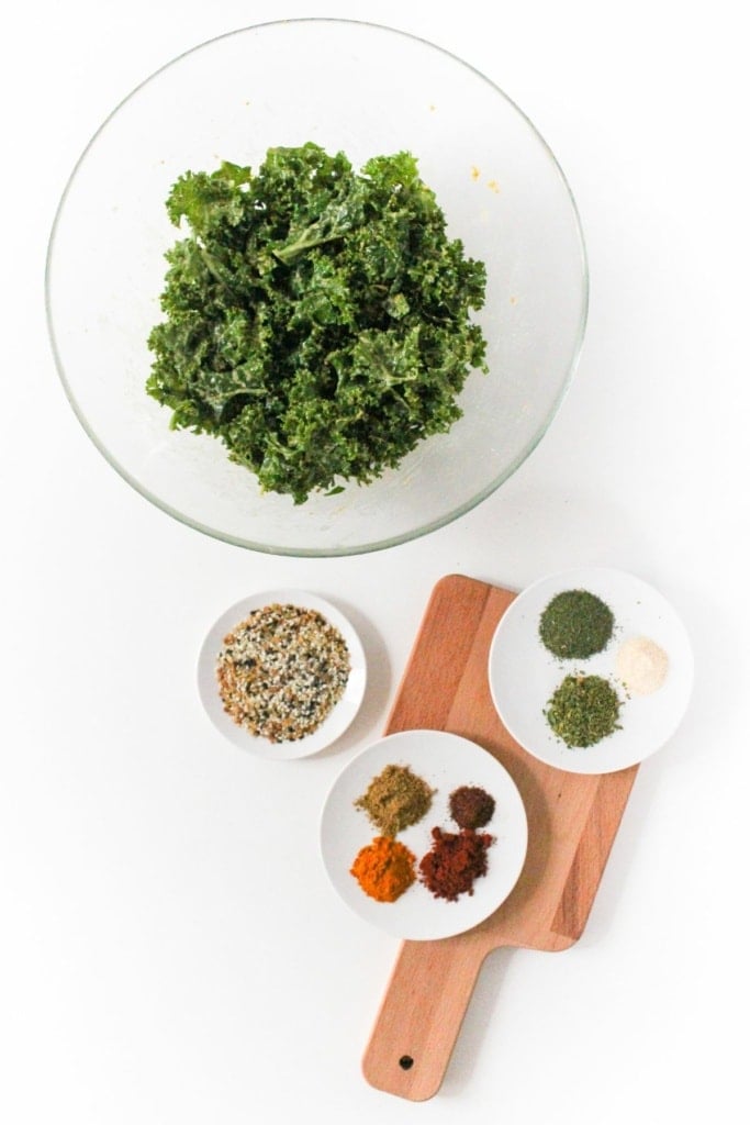 massaged kale in a glass bowl with small plates of seasonings beside it