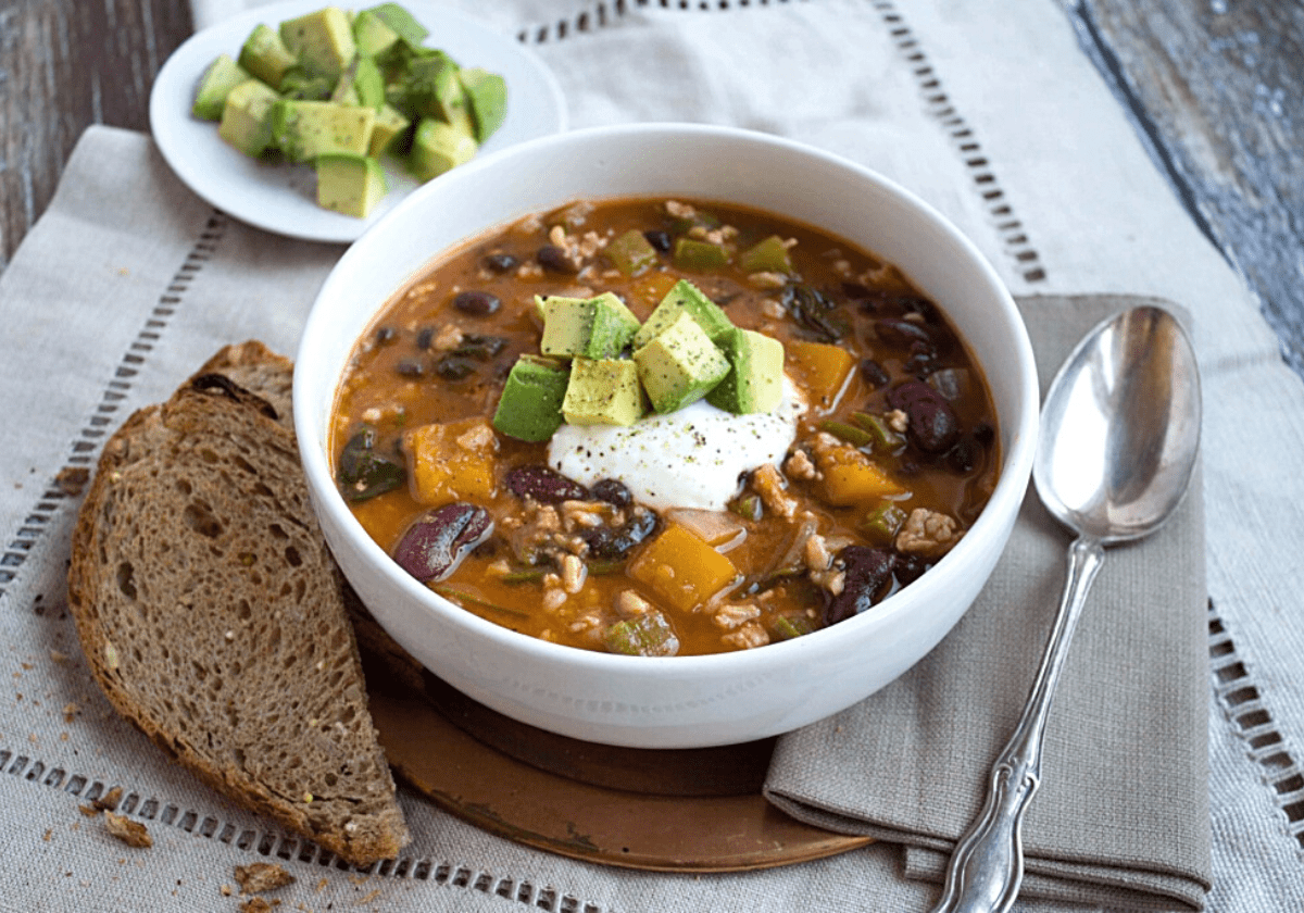 butternut squash turkey chili in a bowl with a slice of bread on the side