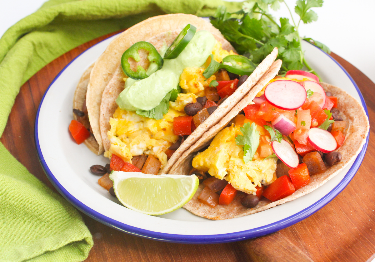 a plate of breakfast tacos with vegetables, black beans, and avocado crema