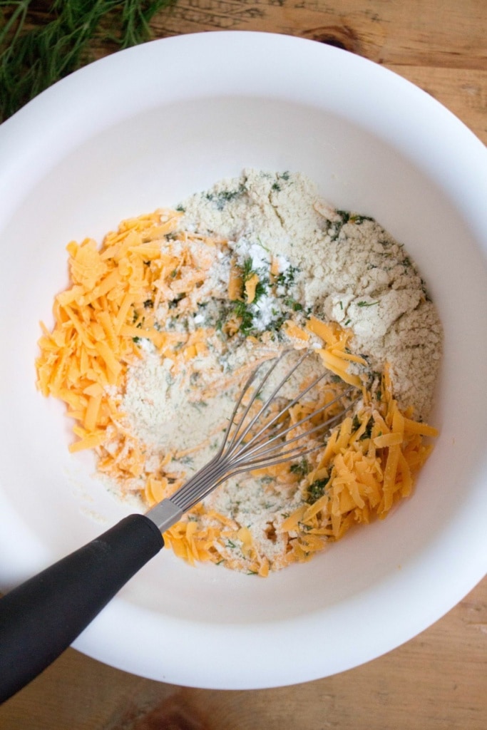 shredded cheddar cheese, gluten free flours, and herbs in a bowl with a whisk