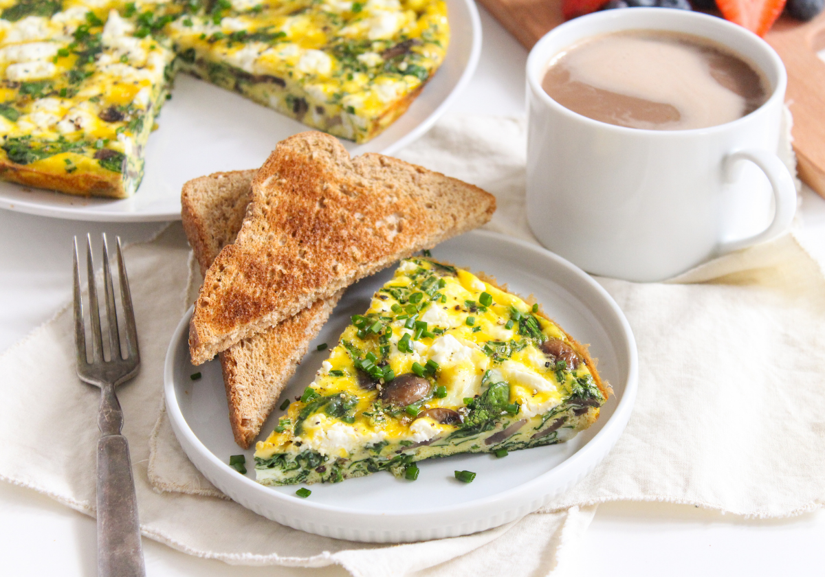 slice of goat cheese frittata on a white place with slices of toast and a coffee cup beside it
