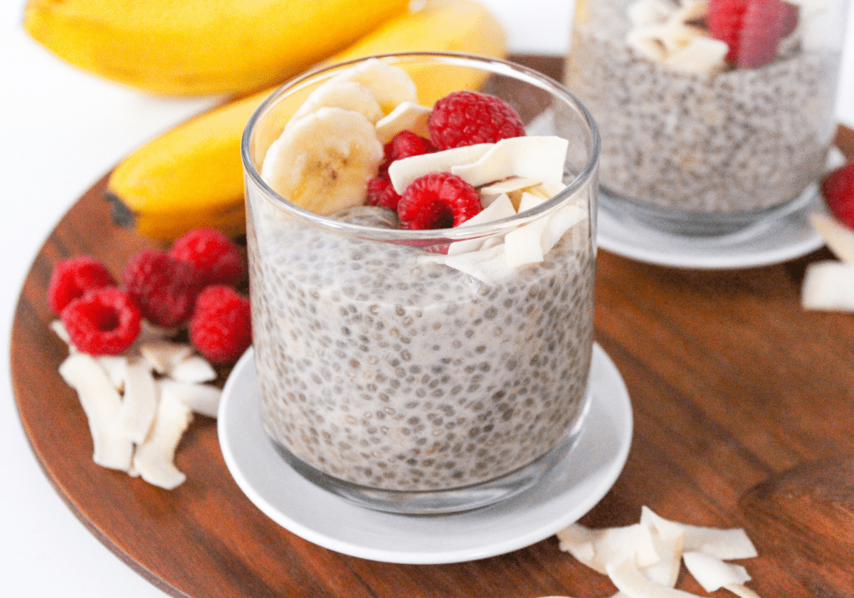 coconut banana chia pudding in a glass with raspberries and banana slices