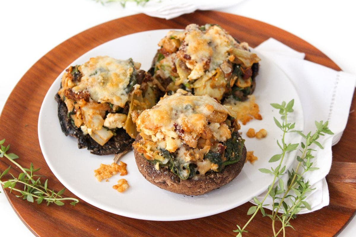 A white plate with baked large portobello mushrooms stuffed with spinach, artichokes, and cheese and sprinkled with fresh herbs.