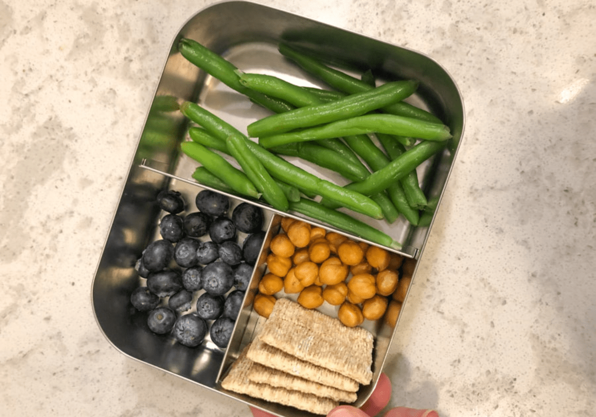 toddler snacks - green beans, blueberries, crackers, and chickpeas - in a metal lunch container
