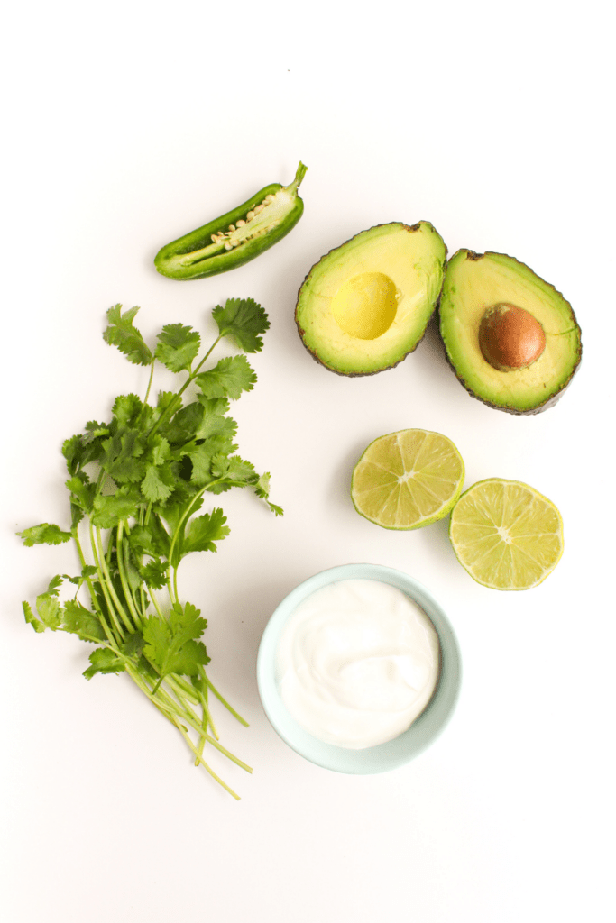 sliced avocado, jalapeno, Greek yogurt, cilantro, and lime slices on a white countertop