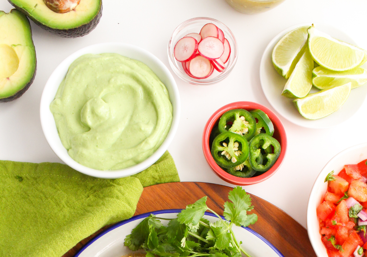 avocado crema in a bowl with limes and sliced avocado next to it