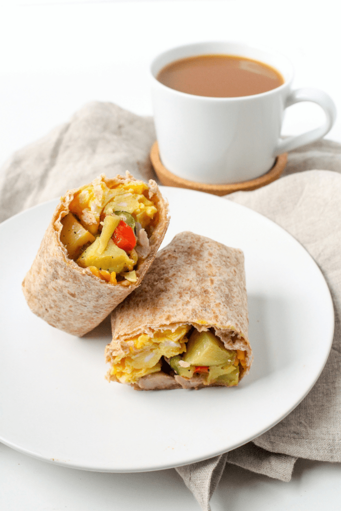 sausage burrito with egg and veggies on a white plate with a white coffee mug behind it