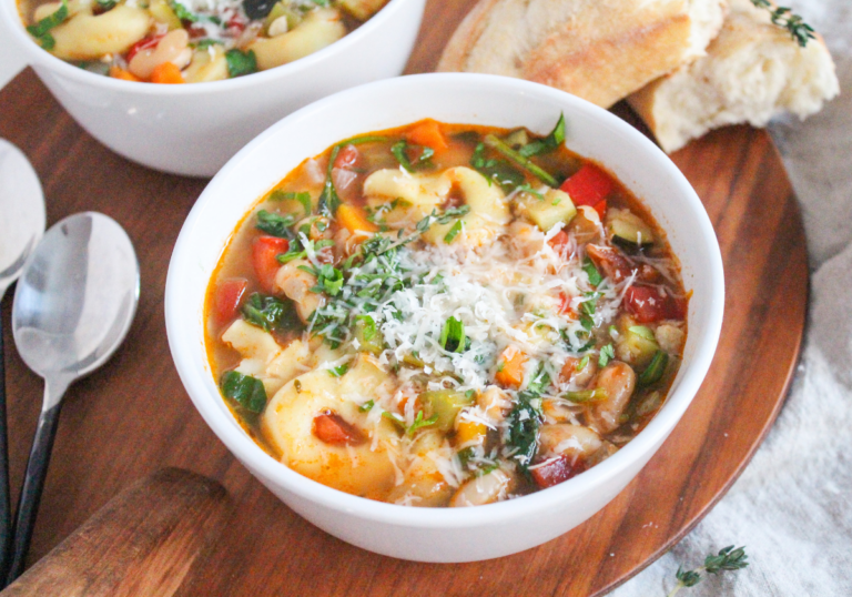 A white bowl filled with veggie-packed tortellini soup and topped with grated parmesan cheese.