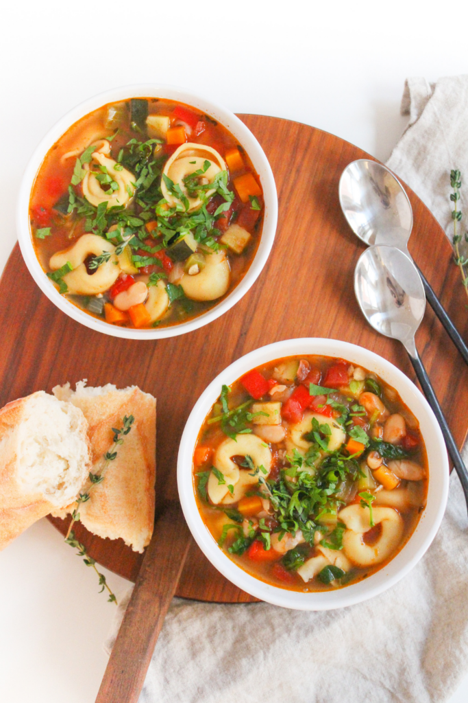 vegetarian tortellini soup in two bowls with crusty bread