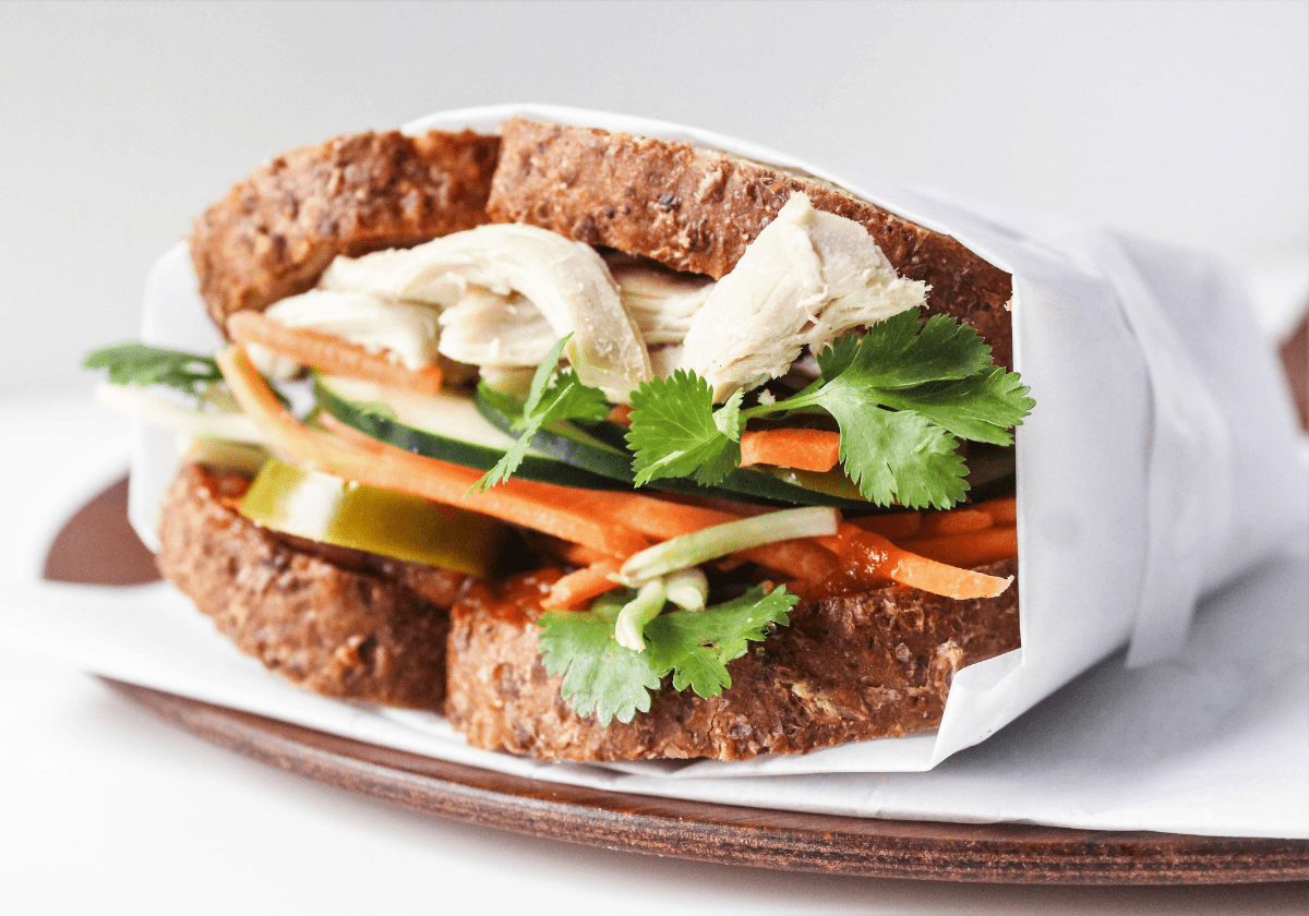 chicken banh mi sandwich wrapped in parchment paper on a wooden platter