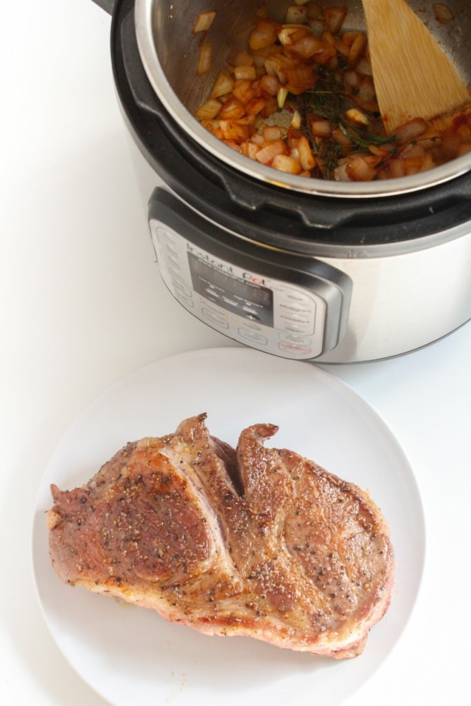 seared pork shoulder on a plate next to an Instant Pot with diced vegetables