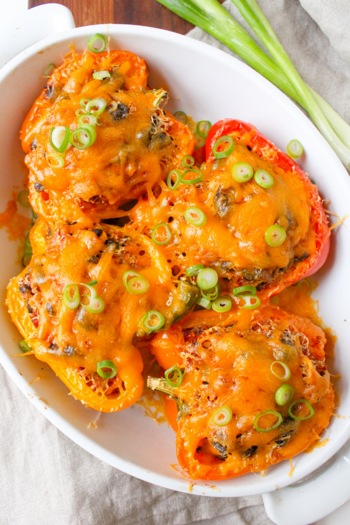 black bean stuffed peppers with quinoa topped with melted cheddar cheese, in a white baking dish