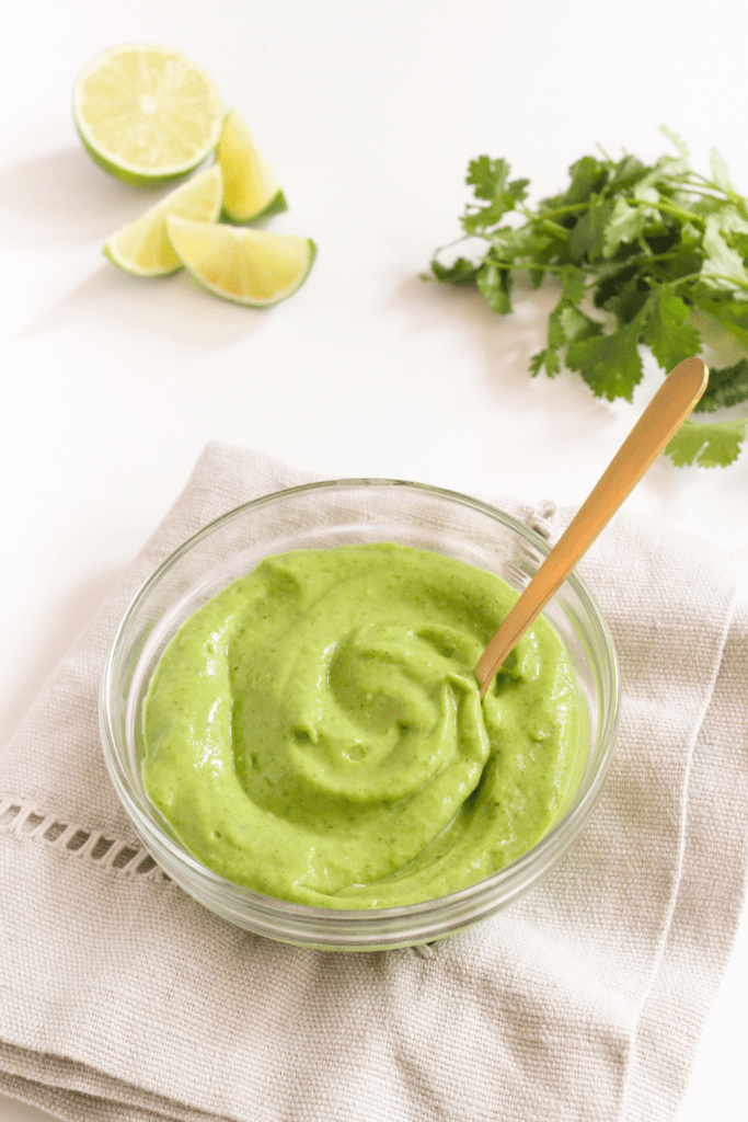 avocado crema in a bowl with sliced limes behind it