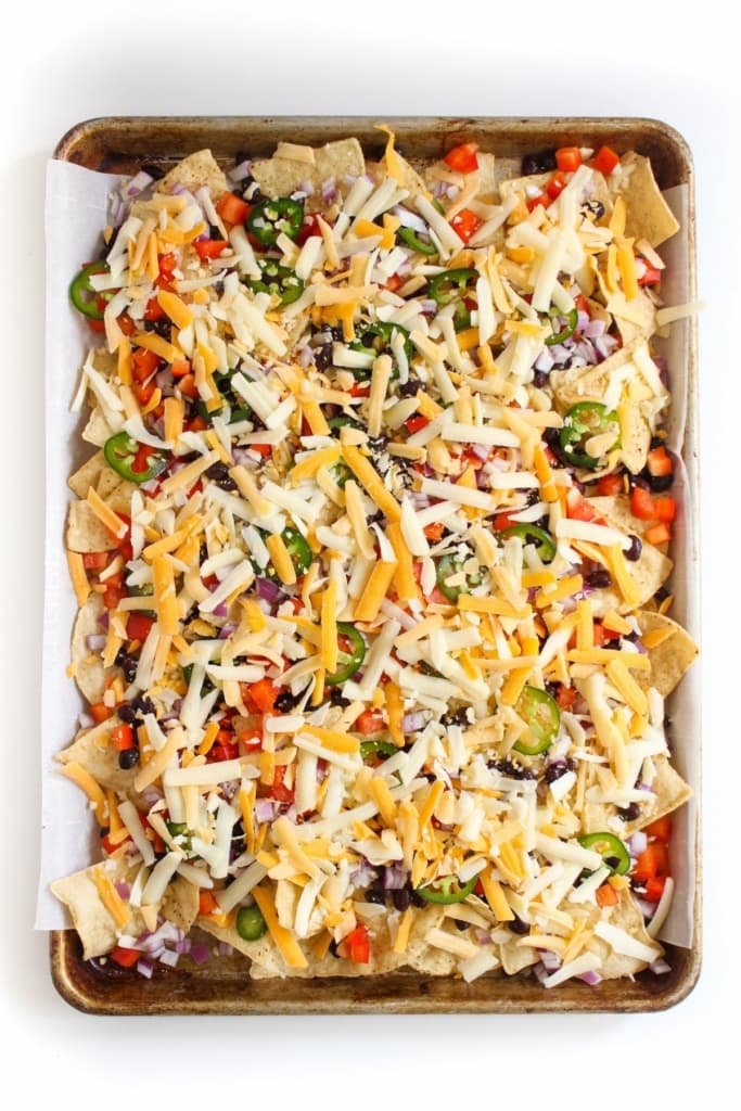 tortilla chips and vegetables with shredded cheese on top on a metal sheet pan