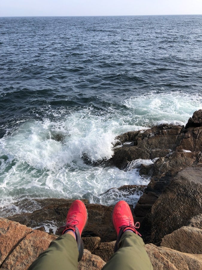 feet dangling over a rock with the ocean below in acadia