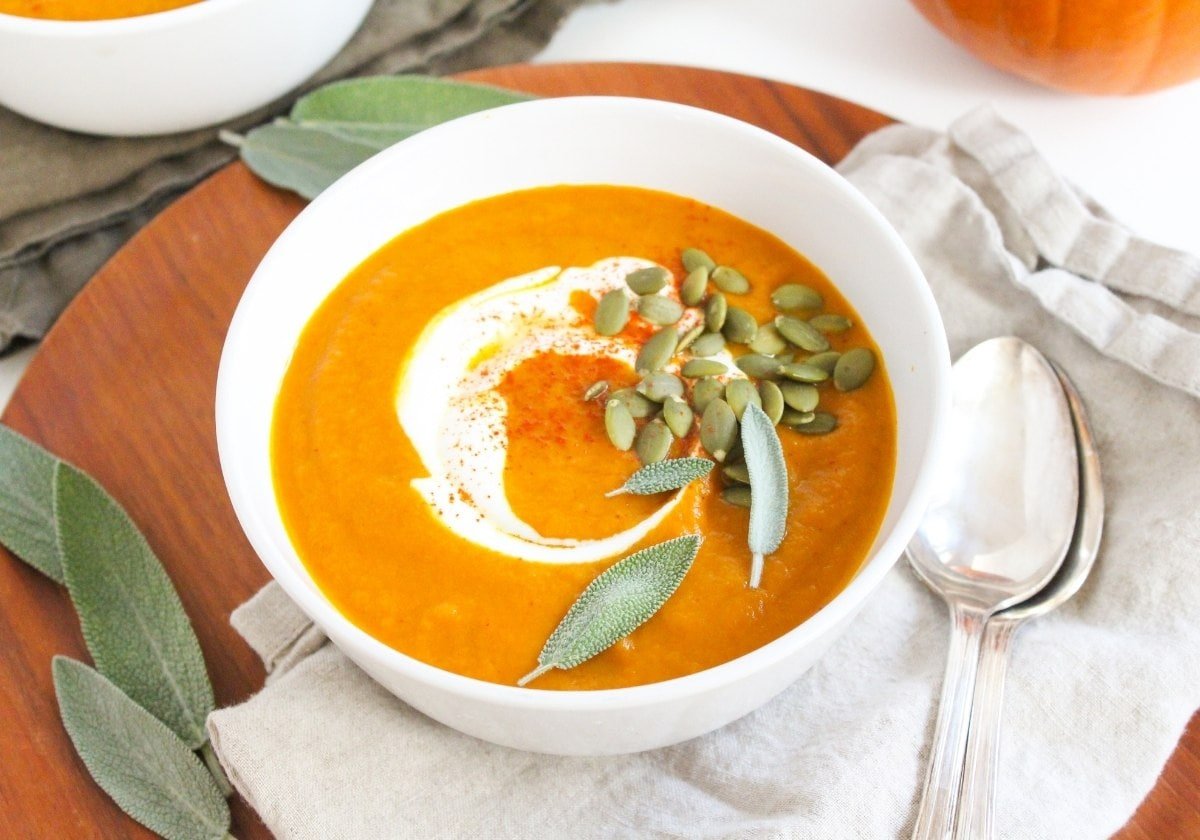 creamy pumpkin carrot soup in a bowl with sage and pumpkin seeds