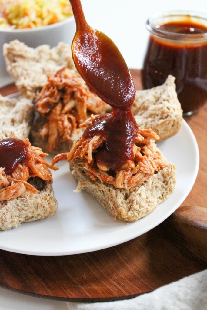 pouring barbecue sauce over pulled chicken sliders on a plate