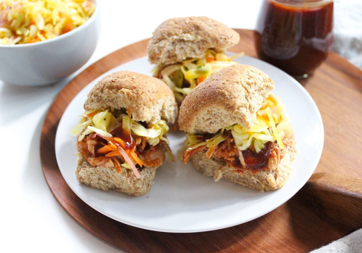 bbq chicken sliders with coleslaw on a plate with a jar of homemade barbecue sauce