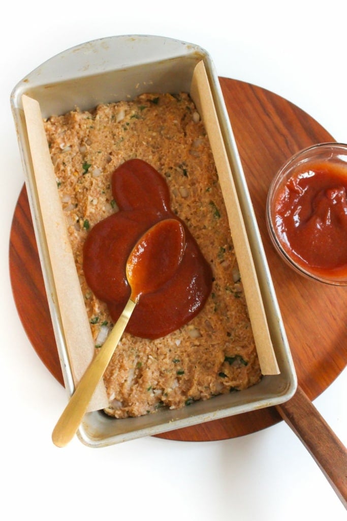 honey dijon glaze being spread over chicken meatloaf in loaf pan