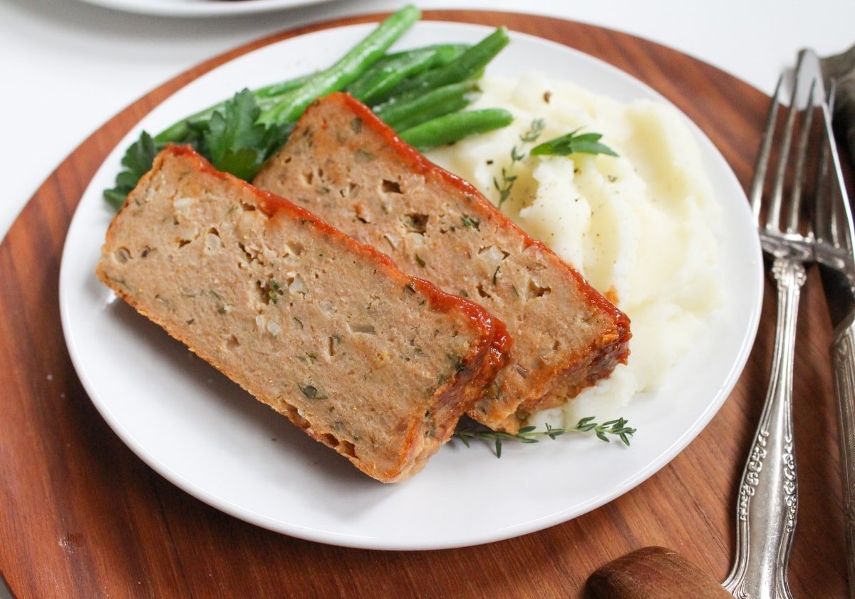 sliced ground chicken meatloaf on a plate with mashed potatoes and green beans