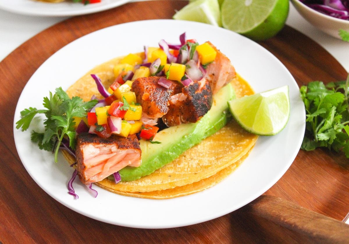 blackened salmon tacos with mango salsa, red cabbage, and avocado slices on a plate