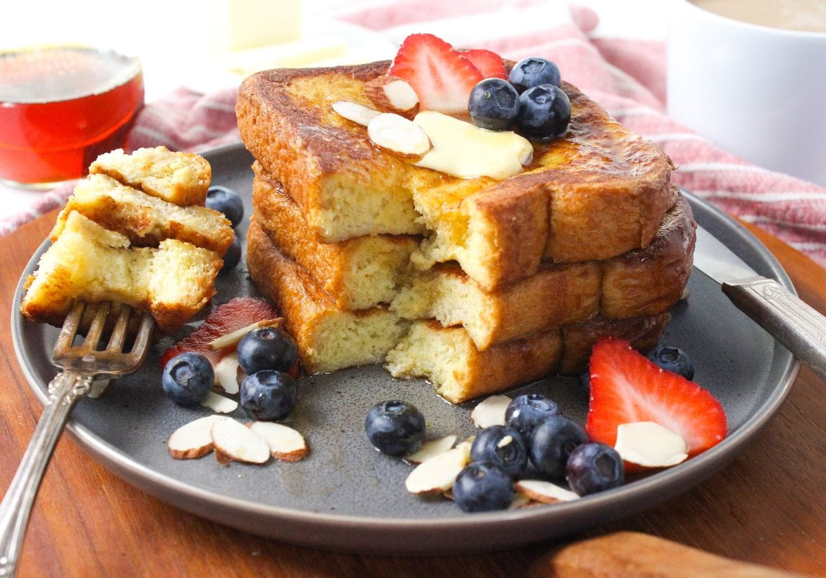 stack of french toast made with almond milk, topped with maple syrup, berries, and sliced almonds