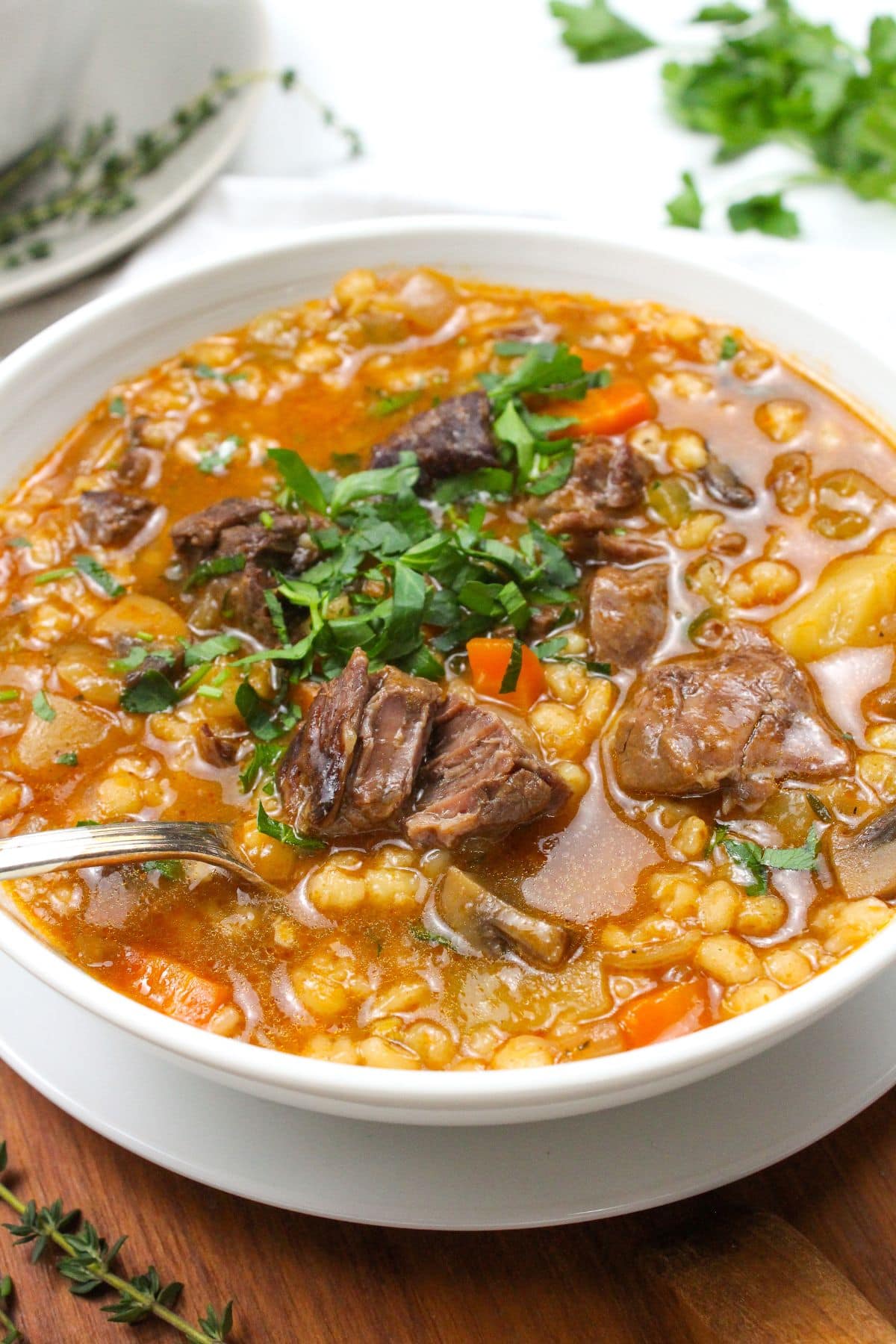 close up of beef and barley soup in a bowl with herbs