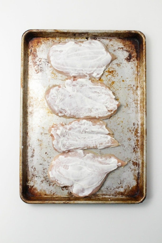 chicken cutlets with plain greek yogurt on top on a metal sheet pan