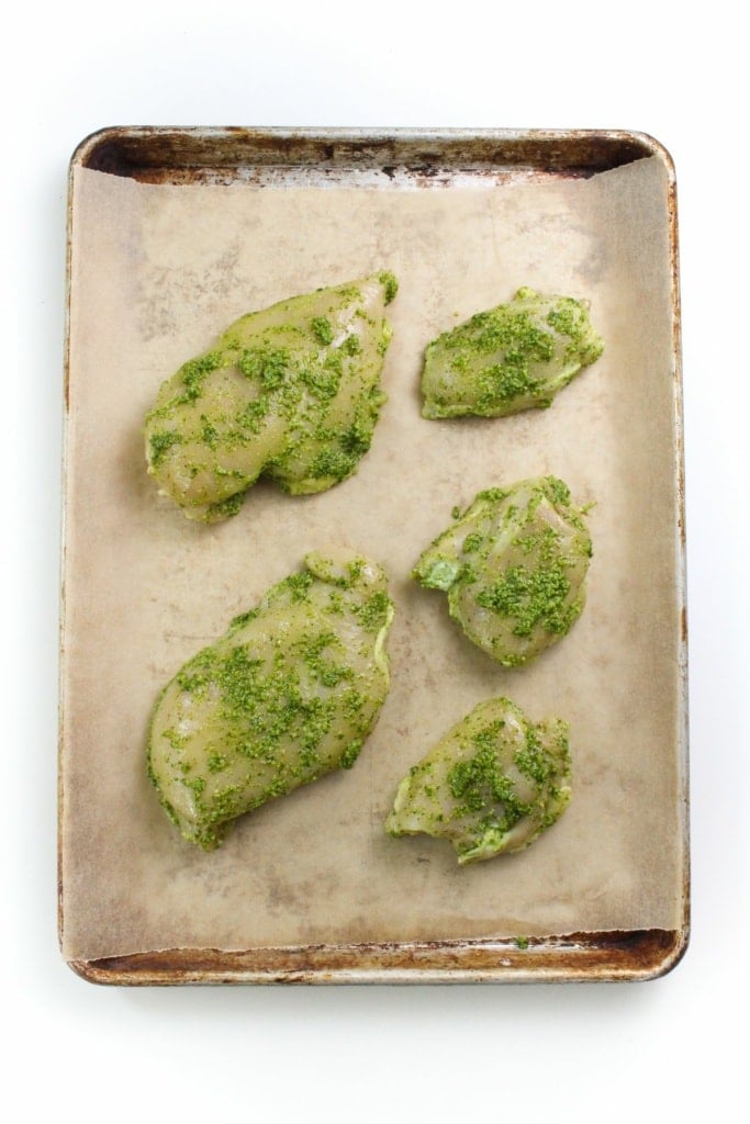 chicken coated in pesto sauce on a sheet pan with parchment paper